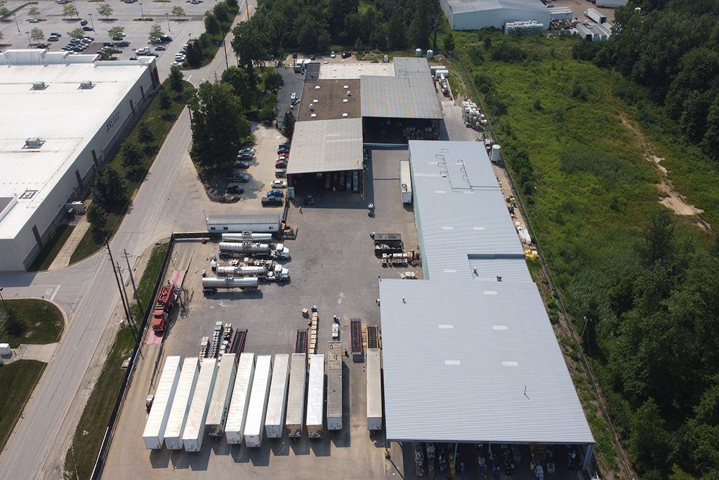 Aerial view of an industrial yard with trucks, trailers, warehouses, and parked equipment near trees.