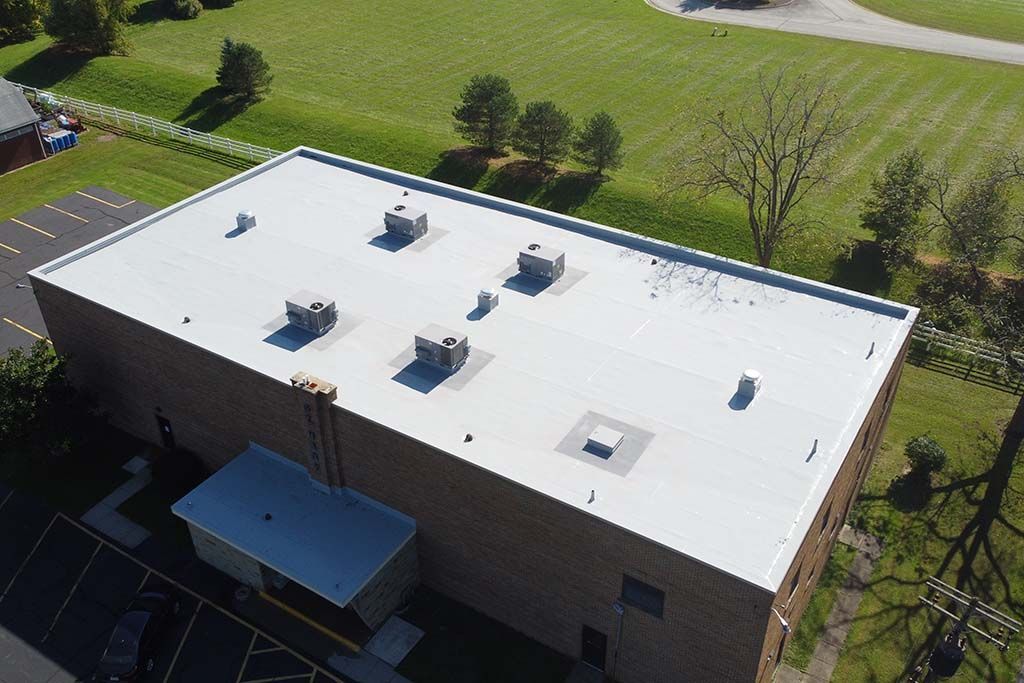 Aerial view of a flat-roof brick building with rooftop vents, beside green lawns and trees