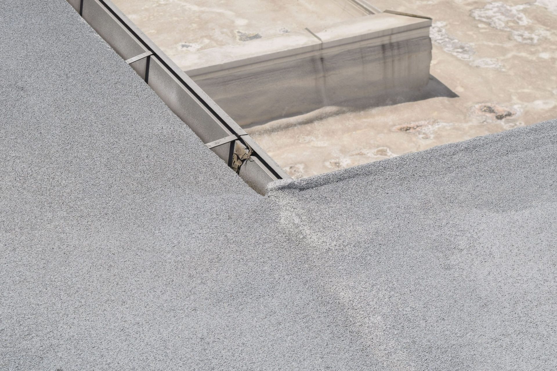 Close-up of a rooftop drain and concrete gutter beside gray gravel roofing.