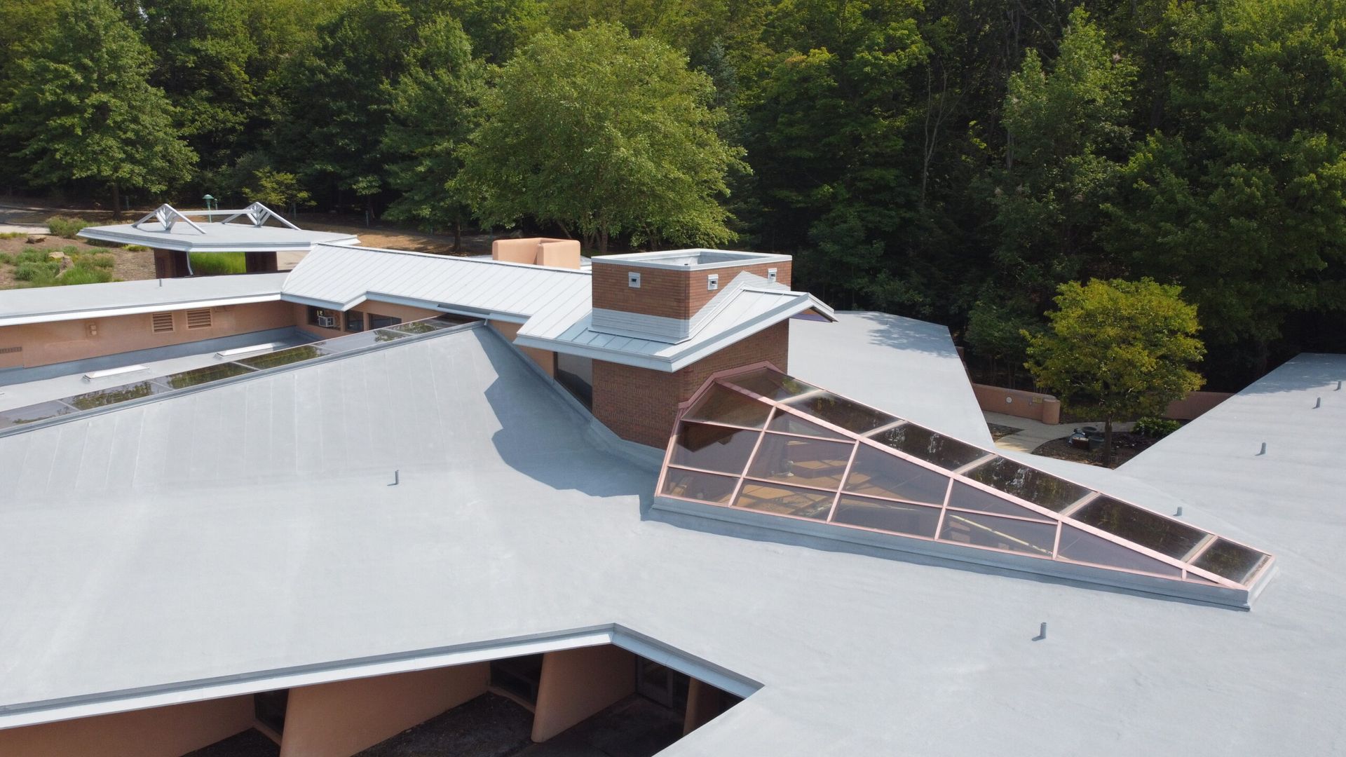 Solar panels on a large gray rooftop surrounded by trees.