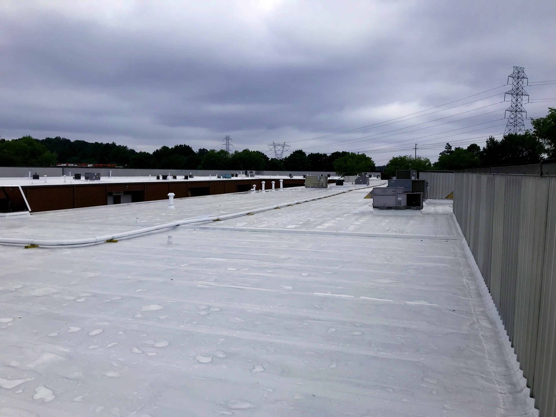 White rooftop with HVAC units under a cloudy sky, bordered by a tall wall on the right.