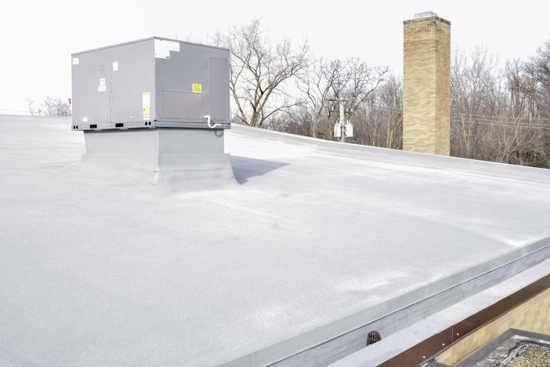 Flat rooftop with gray HVAC unit and tan chimney under a pale winter sky