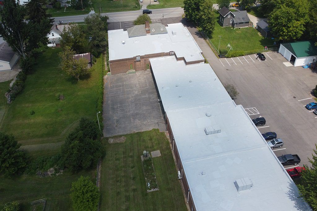 Aerial view of a large white-roofed building beside a parking lot and green lawns.