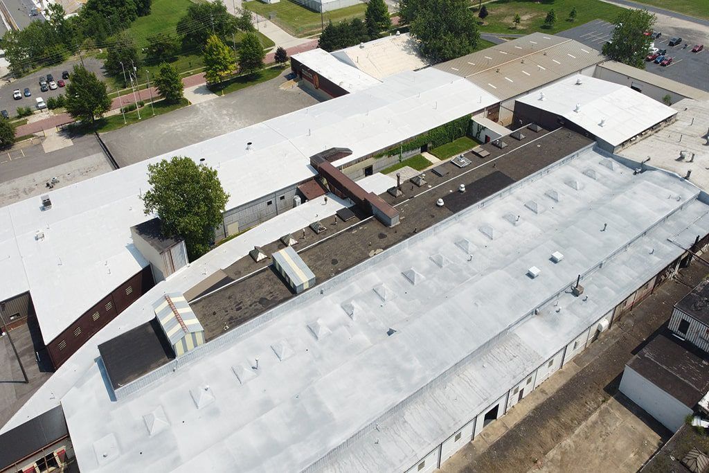 Aerial view of a large white-roofed building complex with surrounding trees and parking areas.