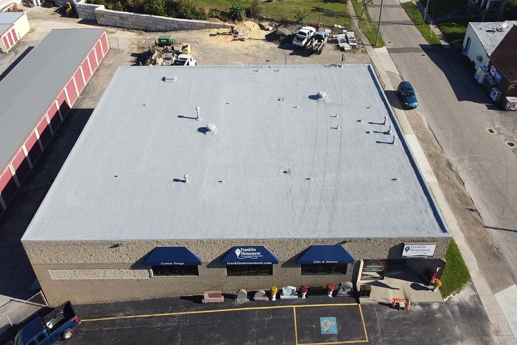 Aerial view of a large white-roofed commercial building with blue awnings and parked vehicles nearby.