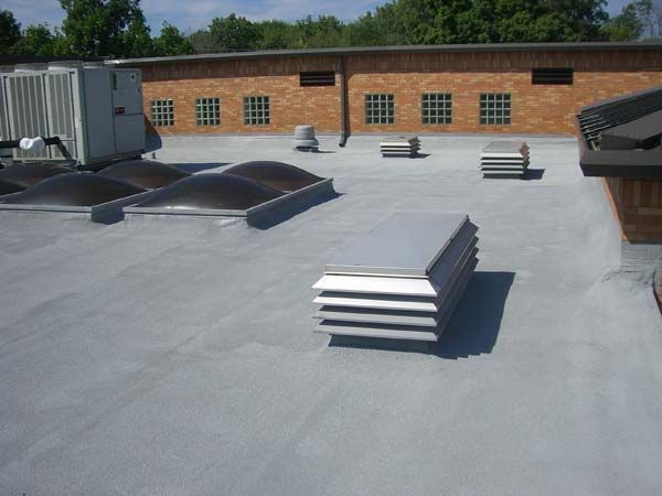 Rooftop with gray membrane, skylights, and ventilation units beside a brick building under a clear sky