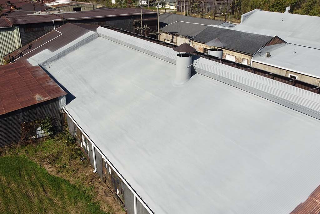 Aerial view of a large gray metal roof surrounded by nearby houses and greenery.