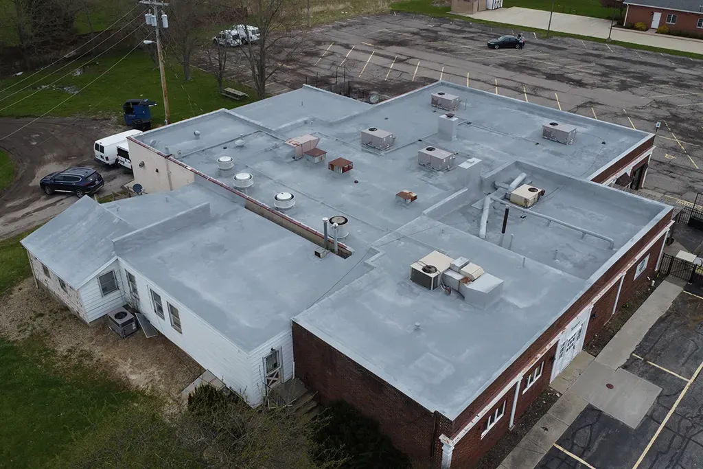 Aerial view of a flat-roofed brick building with HVAC units and parking lot.