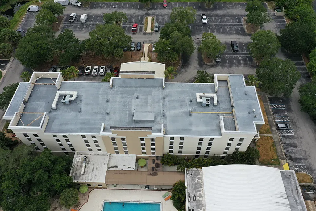 Aerial view of a beige apartment building with a rooftop and pool in a parking lot area