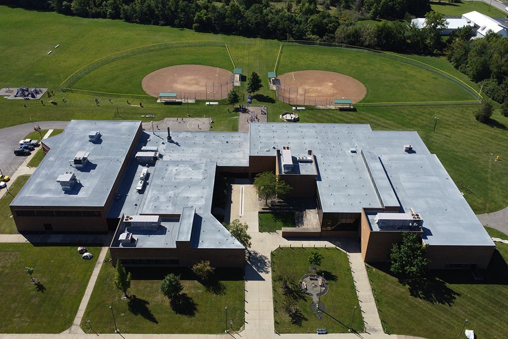 Aerial view of a school building with two baseball diamonds behind it and green lawns around it