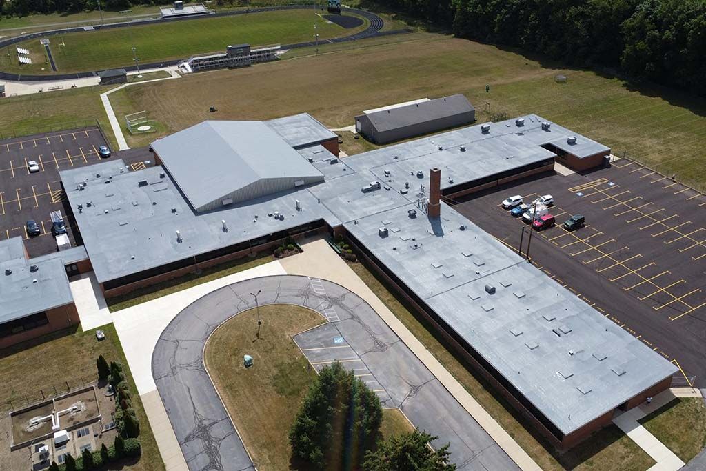 Aerial view of a large gray-roofed building with a curved driveway and parking lot
