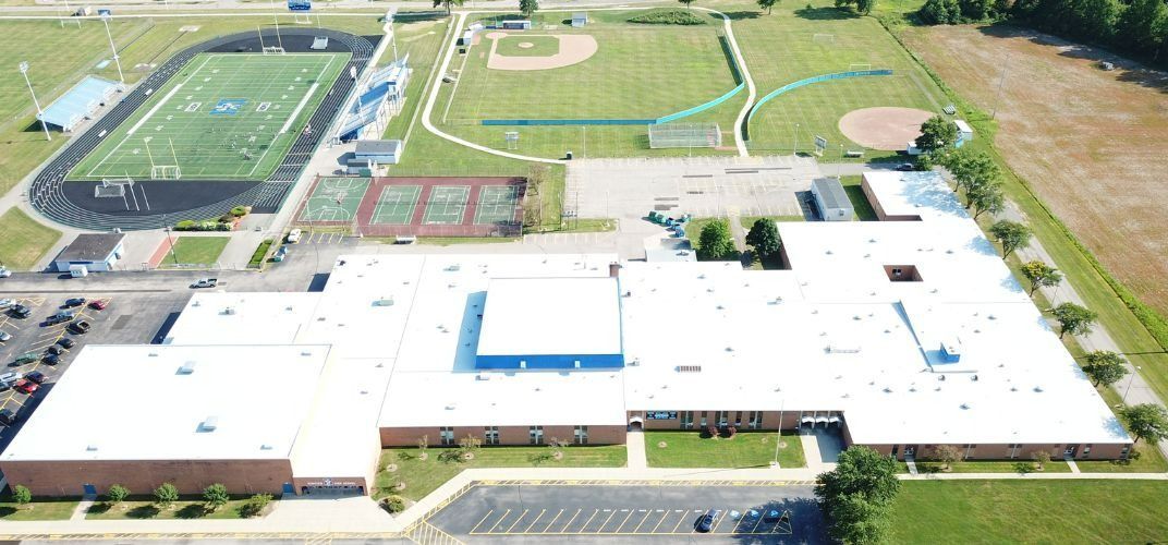 Aerial view of a white-roofed school campus with sports fields and parking lots nearby