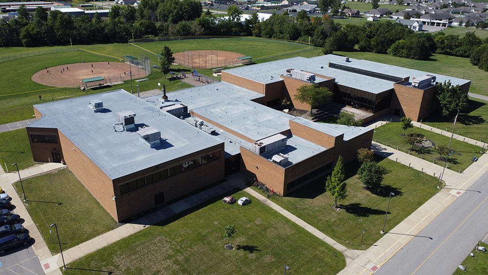 Aerial view of a brick school campus with sports fields, parking lot, and trees.