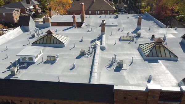 Aerial view of a white flat rooftop with skylights, vents, and chimneys on a brick building.