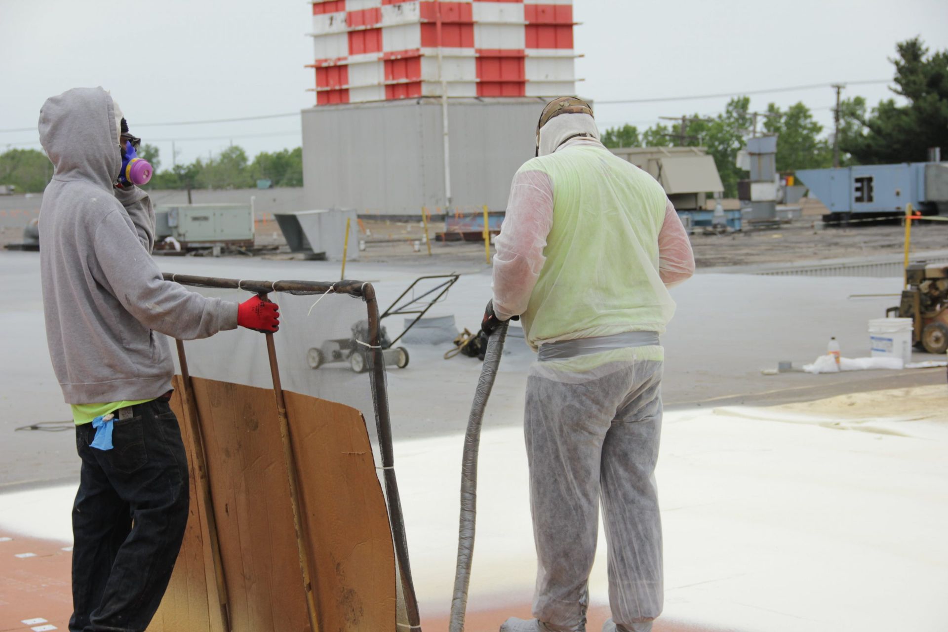 Two workers in safety gear handle a large hose at a wet construction site.