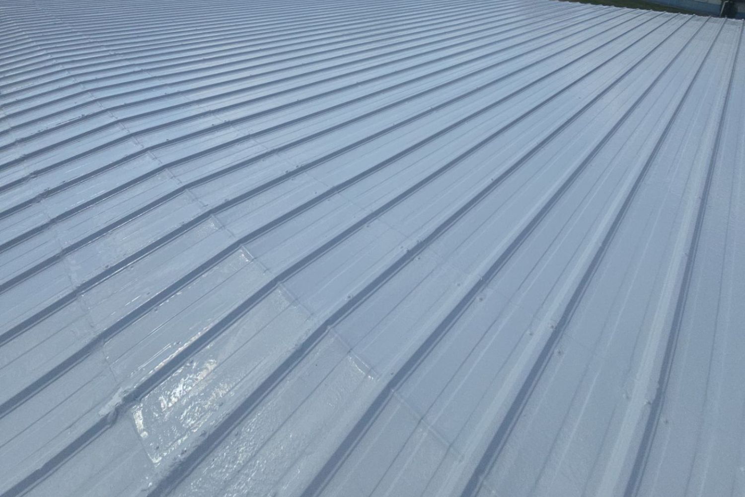 Blue-gray corrugated metal roof viewed from above, with light reflections and parallel ridges