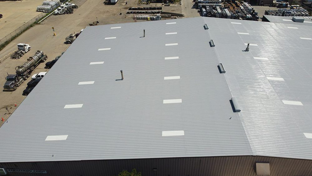 Aerial view of a large white industrial roof with vents and skylights in a dusty lot