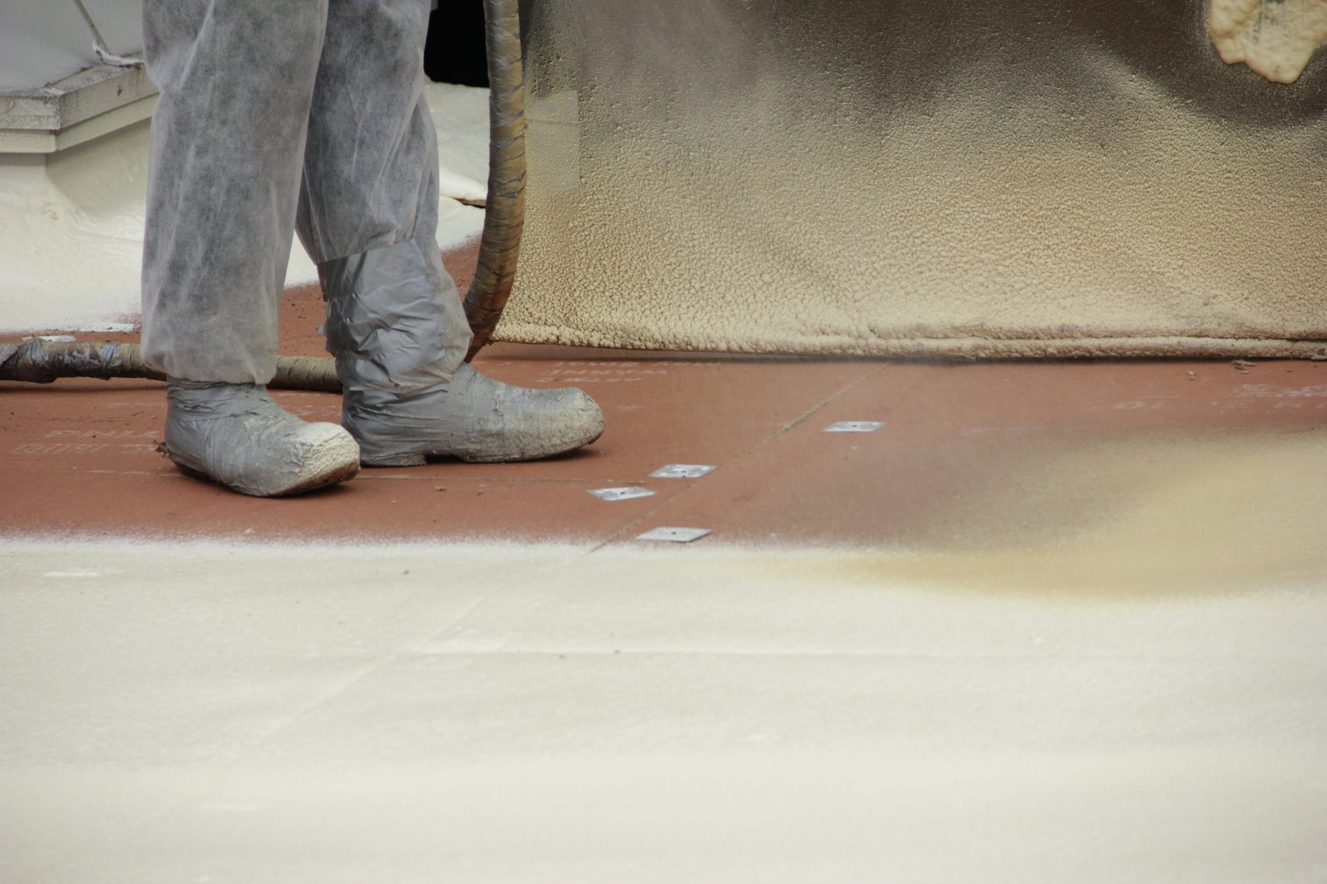 Person in gray pants and boots standing on a reddish floor near a textured wall.