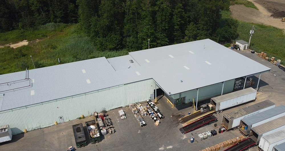 Aerial view of a large white-roofed warehouse with loading docks, trucks, and pallets in an industrial yard