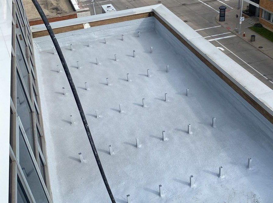 Rooftop with a white membrane and evenly spaced metal anchors beside neighboring buildings.