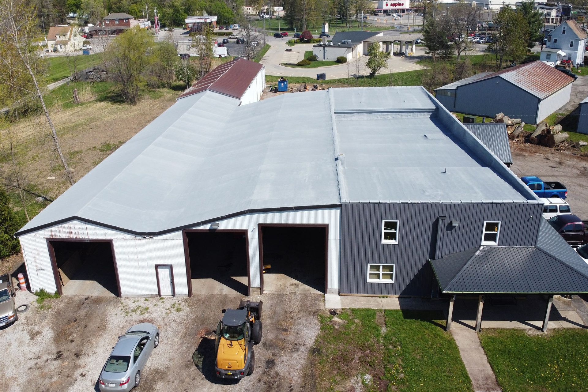 Aerial view of a large gray-roofed barn with open entrances, a tractor, and a small covered porch.