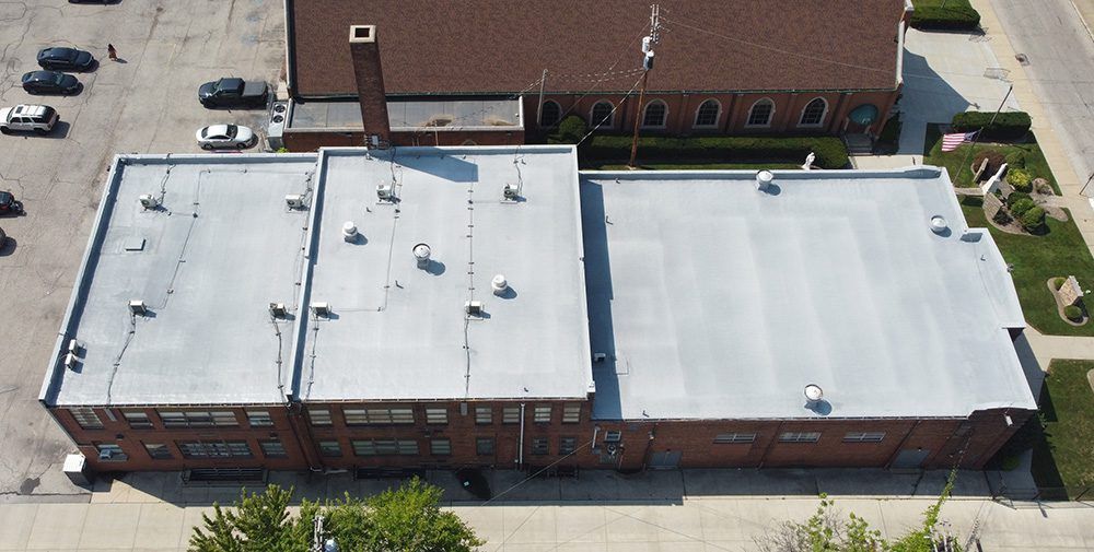 Aerial view of a flat-roofed brick building with white rooftop and adjacent parking lot