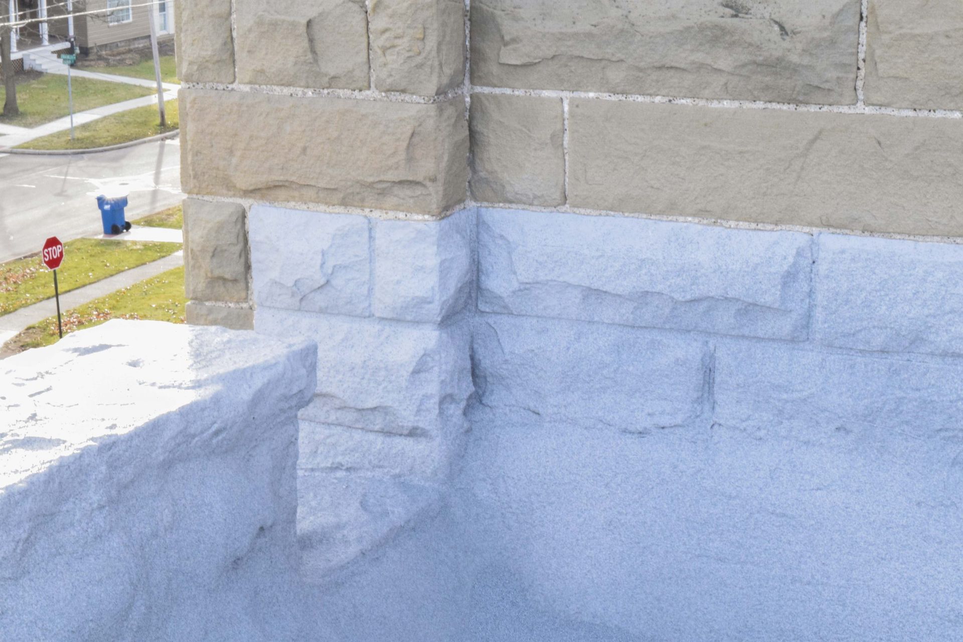 Partially painted stone house exterior with white paint on the lower wall near a sidewalk