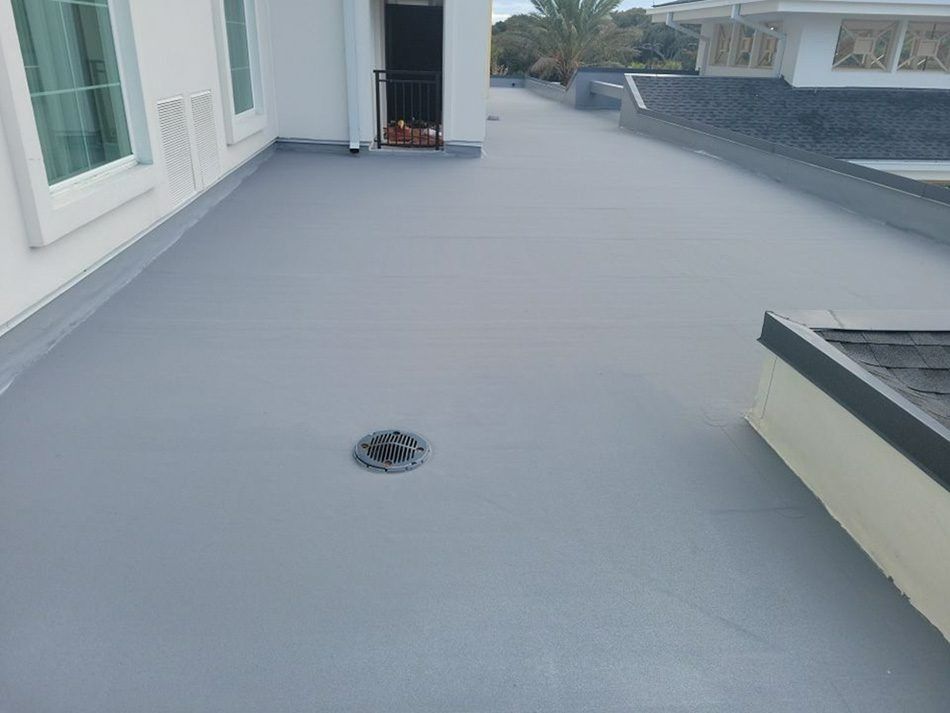 Empty gray rooftop deck with a drain and low parapet walls beside a white building