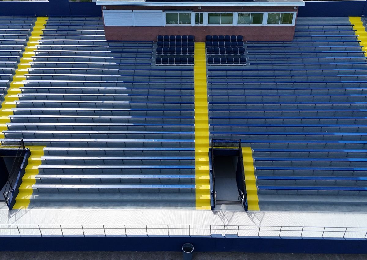 Empty blue stadium bleachers with yellow stairs and central aisle