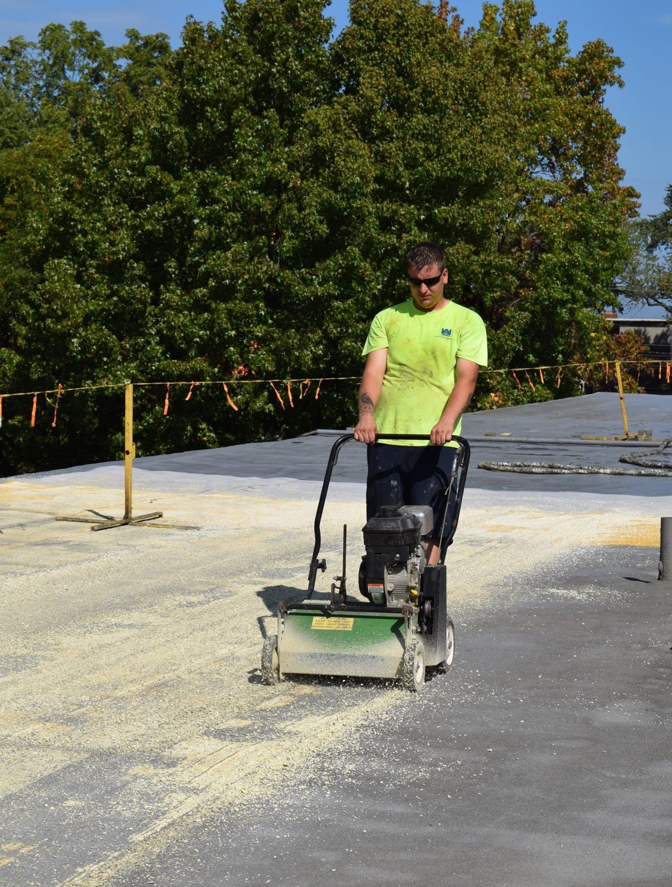Worker operating a pavement machine on a sunlit outdoor surface