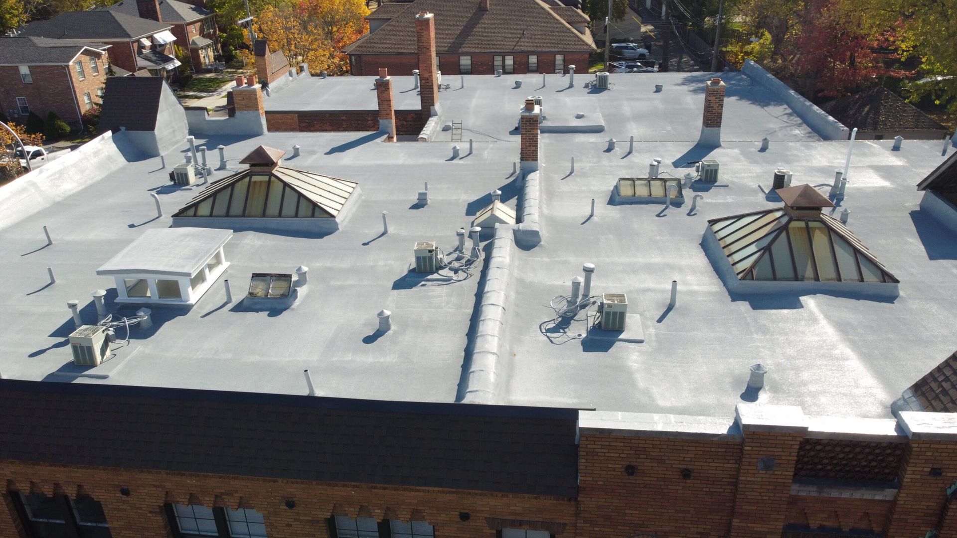 Aerial view of a flat white rooftop with skylights, vents, and small rooftop structures.