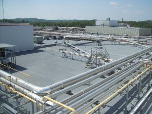 Industrial rooftop with large silver pipes and equipment against a clear sky
