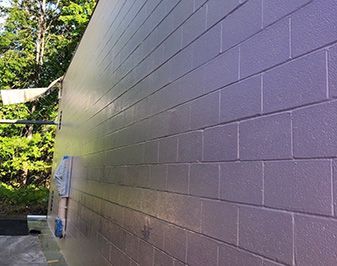 Gray cinderblock wall with a small utility box outdoors beside green trees