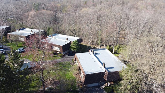 Aerial view of three houses surrounded by leafless trees in a wooded area.