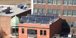 Rooftop solar panels on a red-brick building beside a green-domed tower in an urban setting