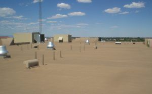 Rooftop with tan gravel, vents and utility units under a blue sky with scattered clouds