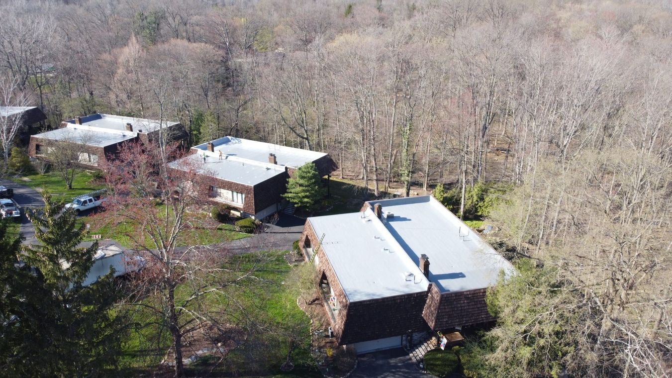Aerial view of three houses surrounded by leafless trees in a wooded area