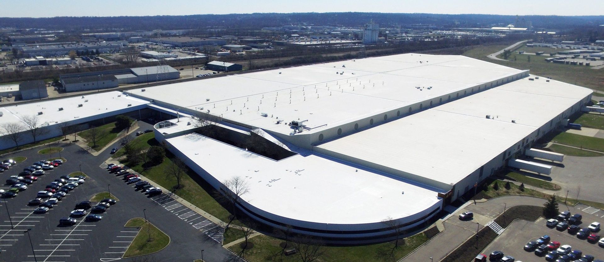 Aerial view of a large white-roofed warehouse complex with parking lots and roads around it