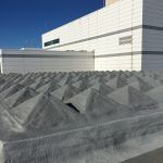Gray geometric rooftop barriers in front of a modern white building under a clear sky