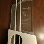 Clear glass award trophy with white base, displayed against a wood background
