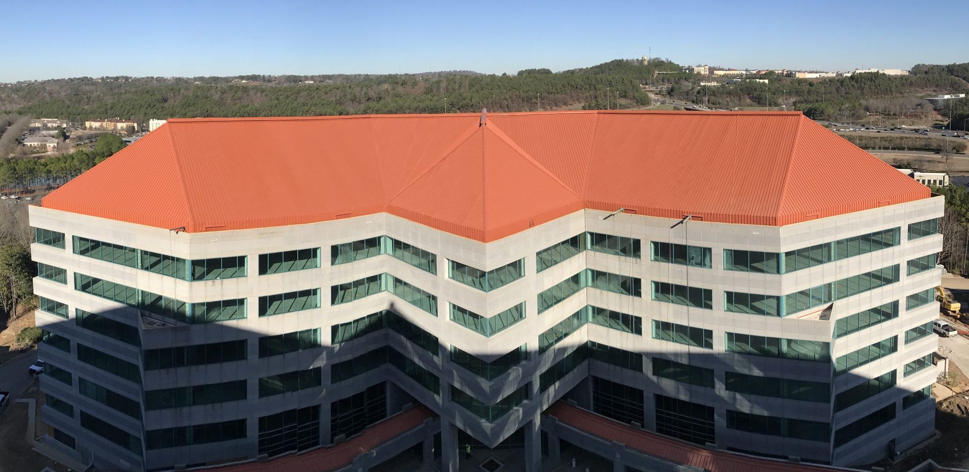 Aerial view of a modern office building with a red-orange roof and white balconies in a hillside setting