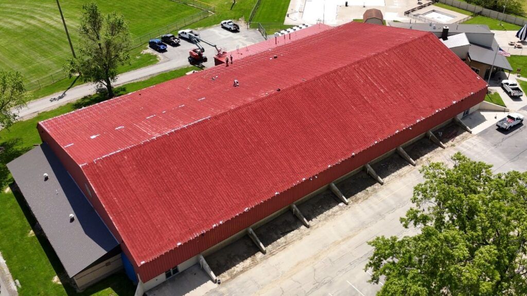 Aerial view of a long red-roofed building with parking lot and trees nearby.