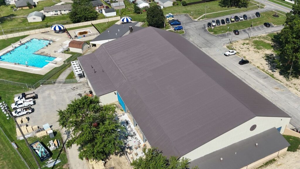Aerial view of a large gray-roofed building beside a swimming pool and parking lot.