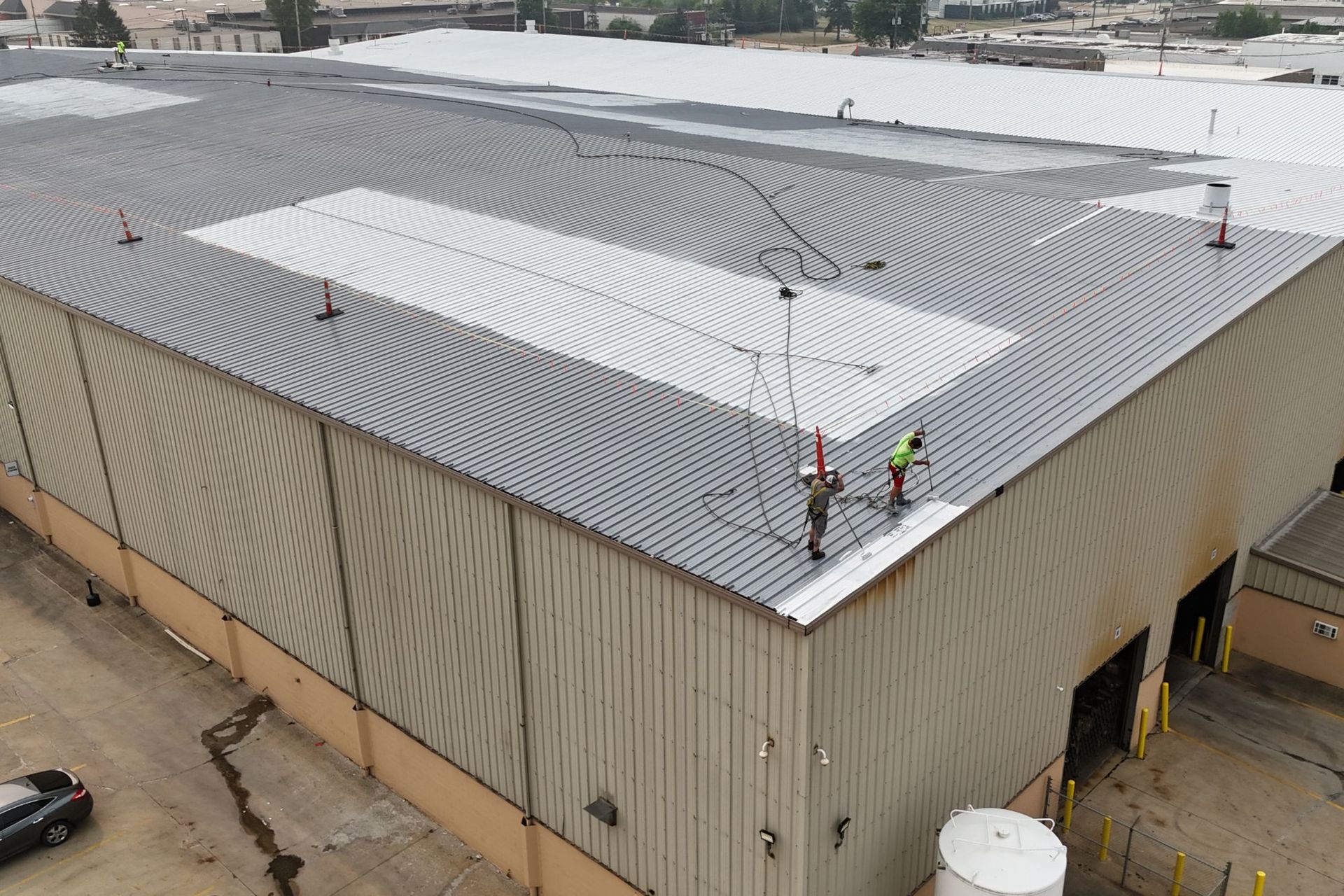 Installing roof coating system - workers tied off when working outside the warning lines. This metal roof is in Bedford, Ohio.