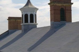 Rooftop with two brick chimneys and a white cupola casting long shadows