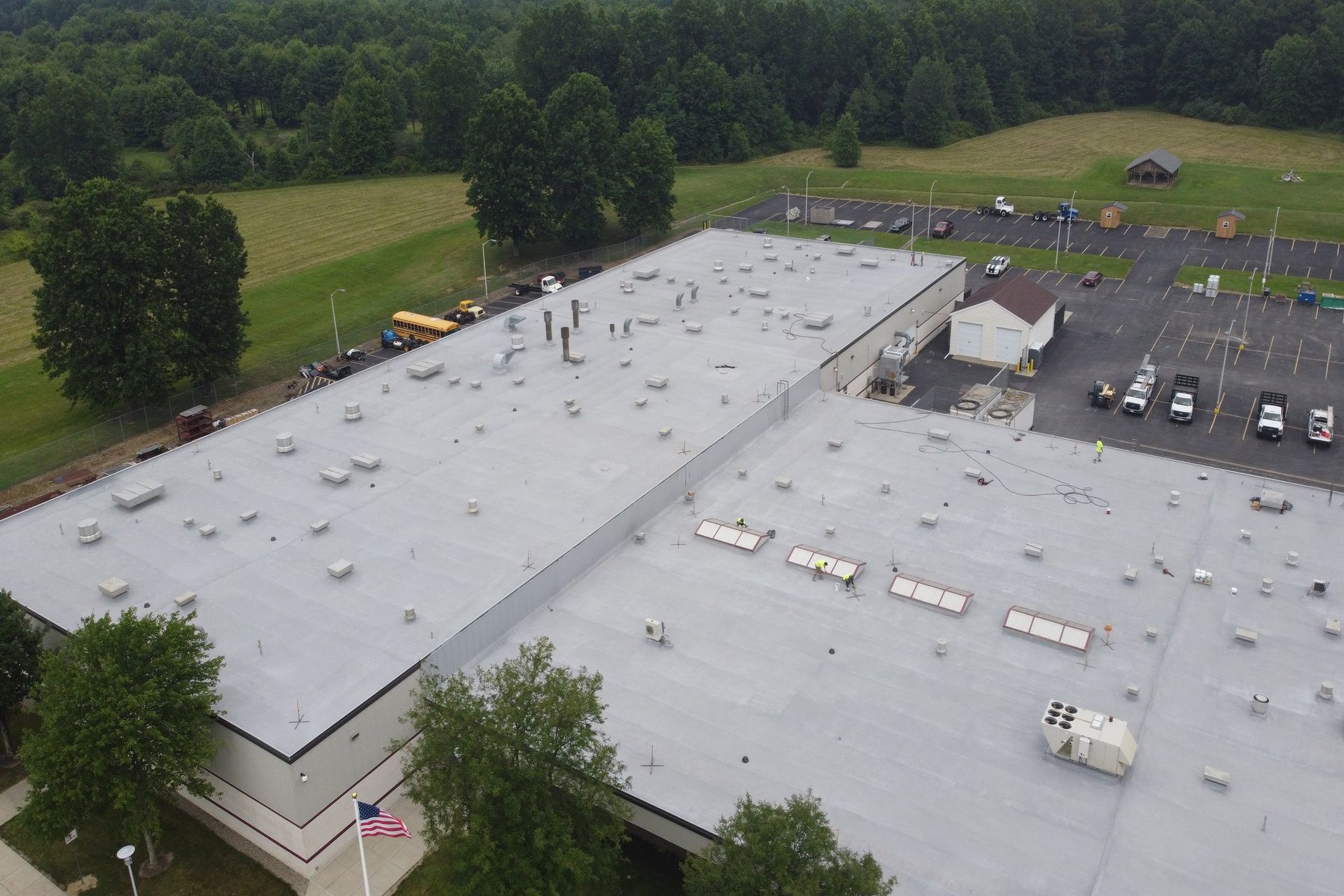 Aerial view of a large gray-roofed building with a parking lot and surrounding trees.