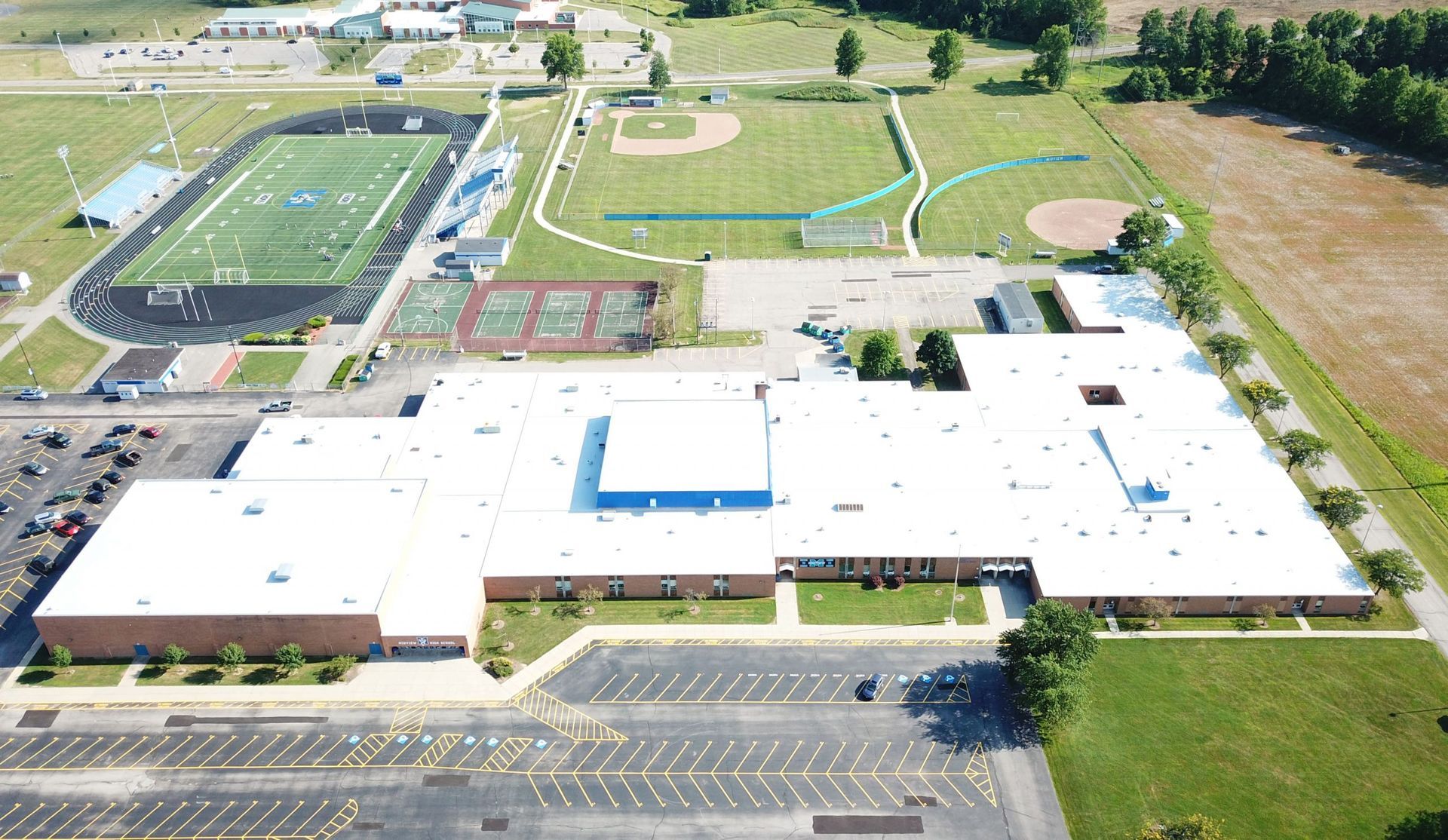 Aerial view of a school campus with buildings, sports fields, parking lots, and grassy grounds.