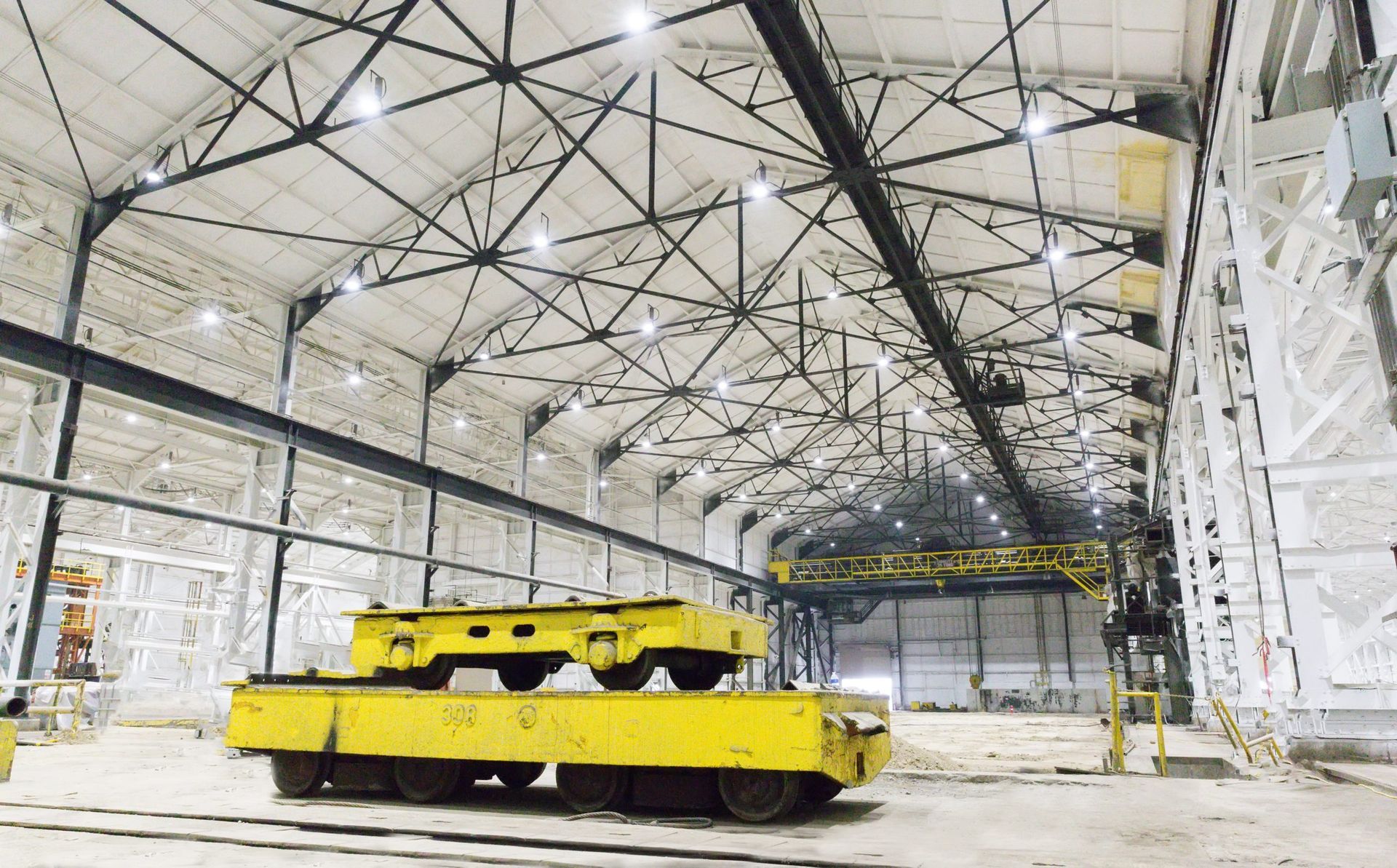 Yellow industrial vehicle in a large warehouse with high steel trusses and bright overhead lights