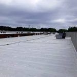 Flat white rooftop with HVAC units, low parapet walls, and cloudy sky in the background