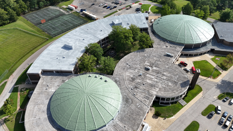 Aerial view of a large industrial building with a white roof and yellow trim in a rural area.